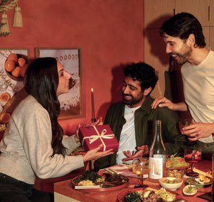 People gathered around a table with food and drinks, one person is presenting a gift.